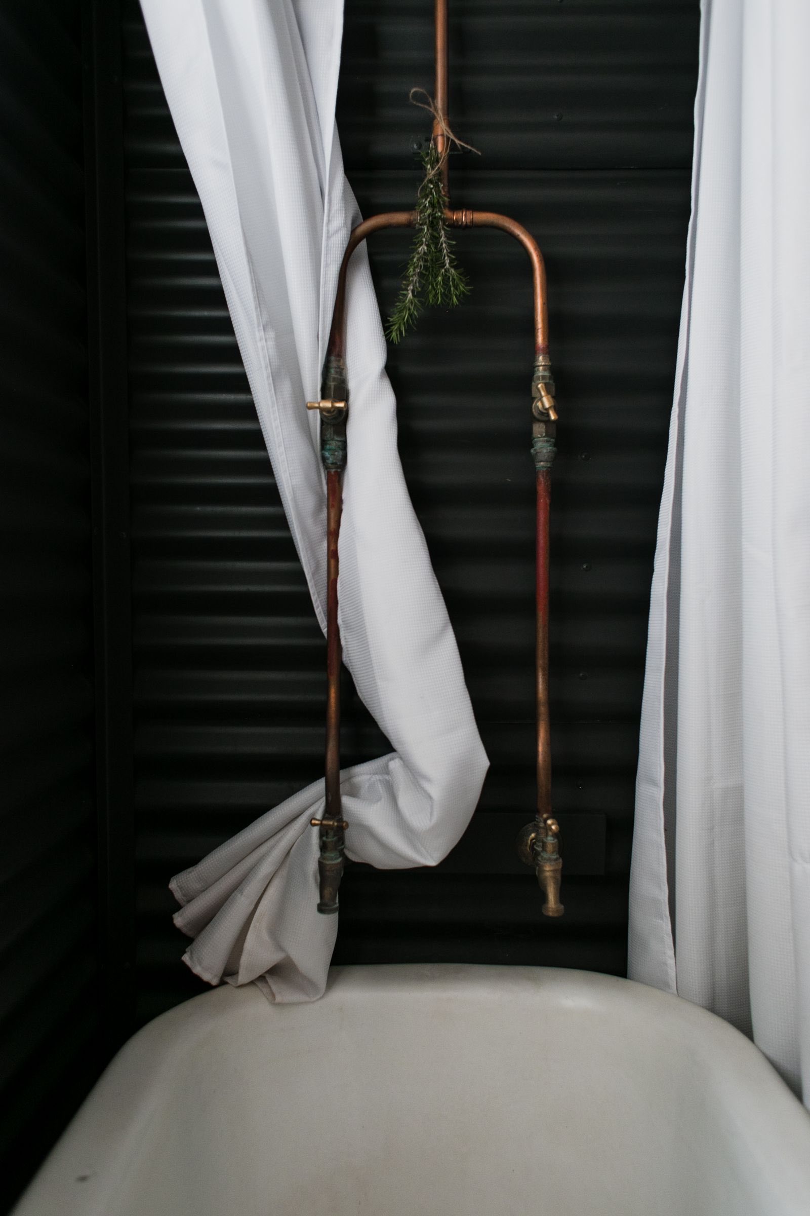 Exposed copper shower pipes with brass valves above a white bathtub
